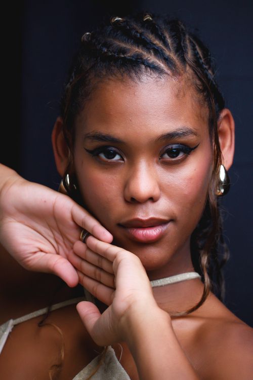 Free Close-up portrait of a woman with braided hair and gold hoop earrings, set against a dark background. Stock Photo