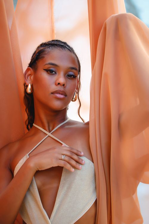 Free Striking portrait of a woman surrounded by flowing, sheer orange fabric, exuding elegance and grace. Stock Photo