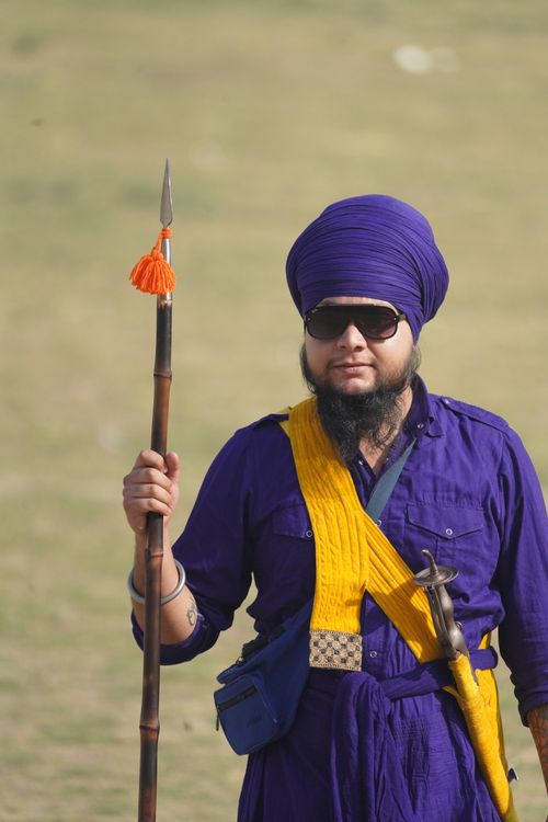 Free A Sikh warrior in traditional attire holding a spear, set outdoors on a sunny day. Stock Photo