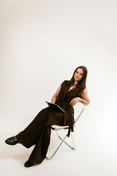 Professional woman in brown suit sitting confidently on a modern chair with a tablet.