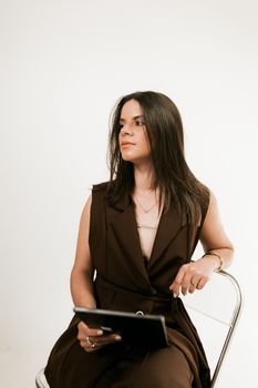 Professional woman sitting on chair holding a digital tablet, projecting confidence.