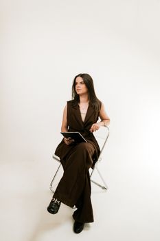 Confident woman in brown attire sitting on a chair in a minimalist studio setting.