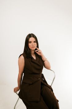 Portrait of a woman in stylish brown attire sitting gracefully on a chair.