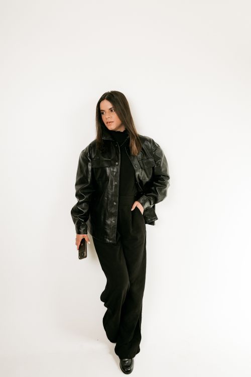 Free Fashionable woman wearing leather jacket and holding smartphone indoors. Stock Photo