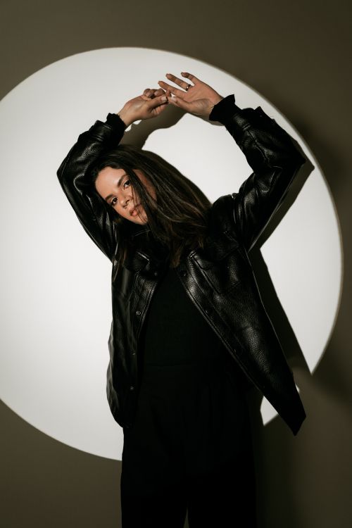 Free A woman in a black leather jacket poses gracefully with dramatic lighting casting shadows. Stock Photo