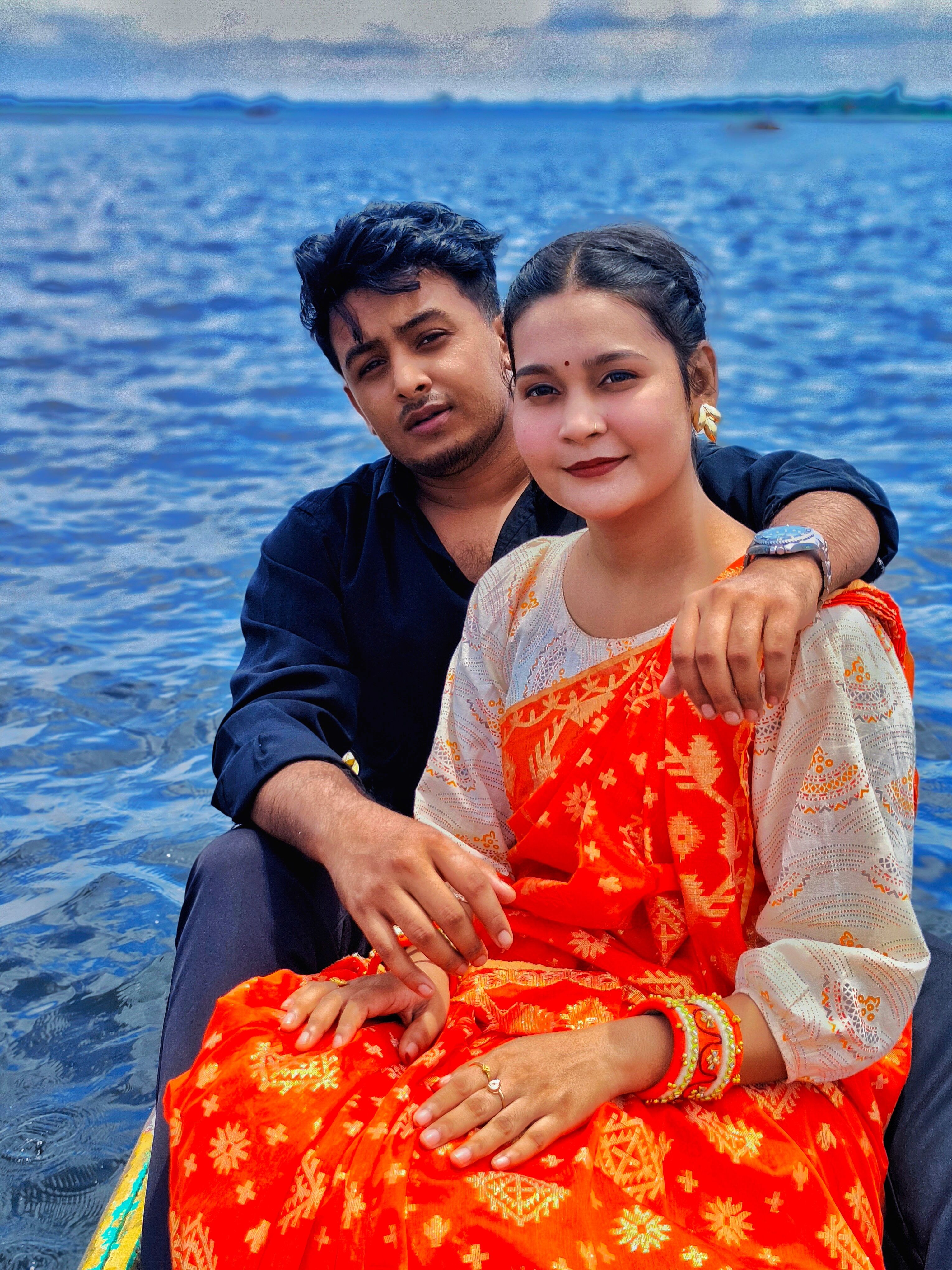 A young couple in colorful attire posing on a boat with a scenic ocean backdrop.