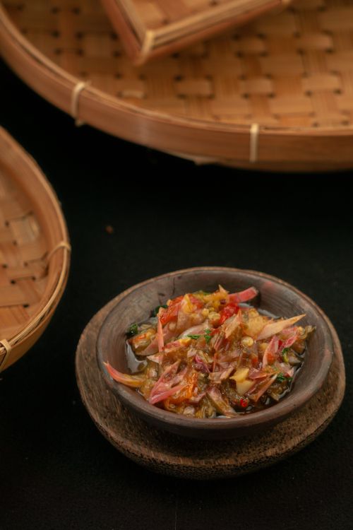 Free Authentic Indonesian sambal served in a rustic wooden bowl with bamboo baskets in the background. Stock Photo