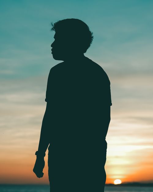 Free Silhouette of a man standing outdoors against a vibrant summer sunset sky. Stock Photo