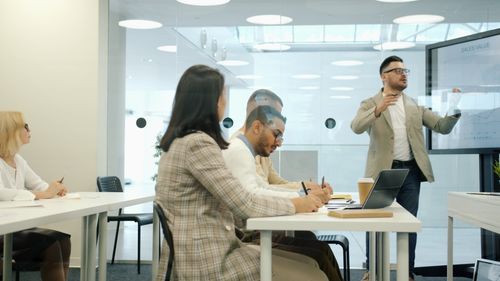 Free Professionals engage in a business presentation within a modern, light-filled office space. Stock Photo