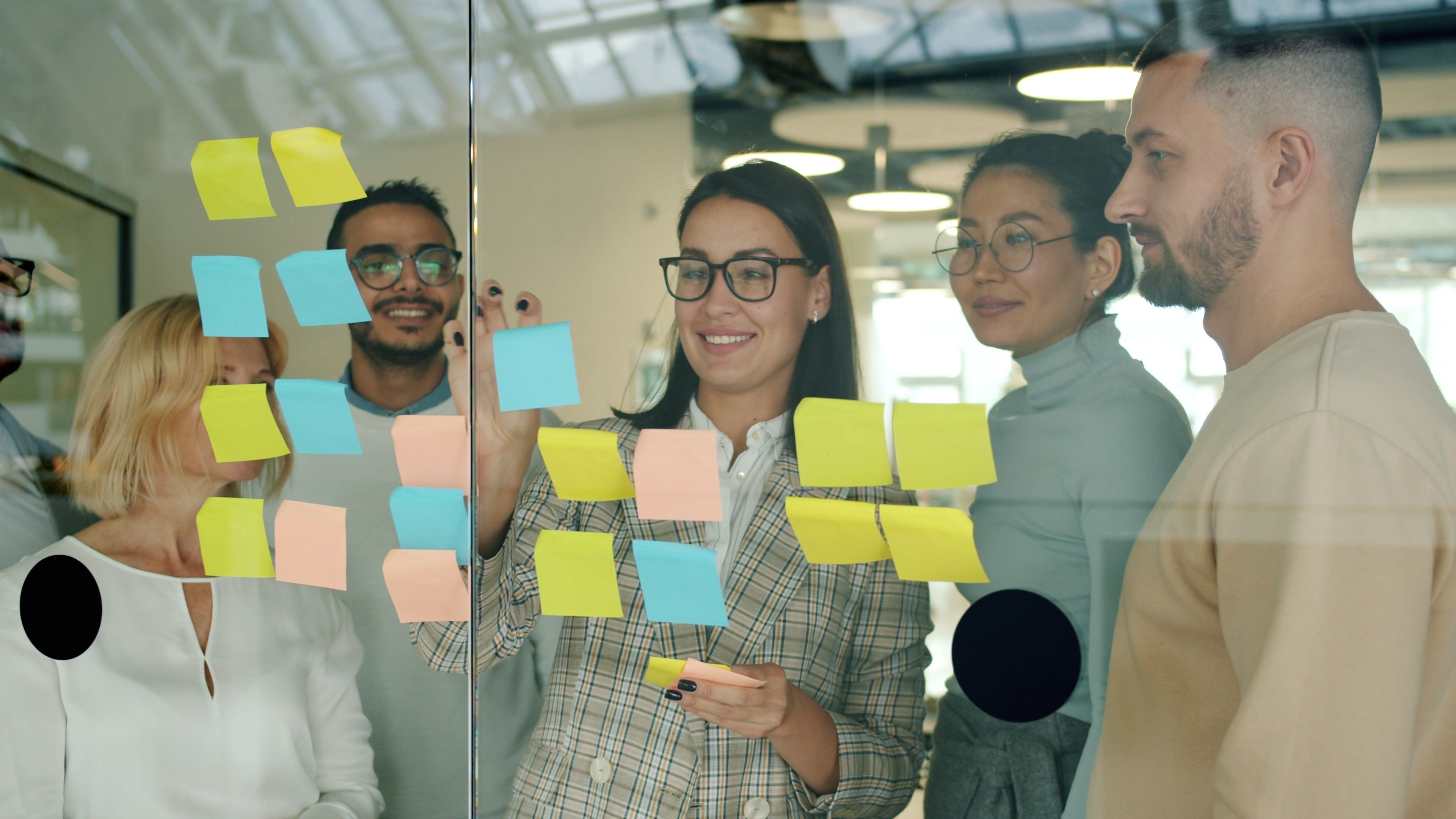 Diverse colleagues collaborating in an office using sticky notes on glass wall.