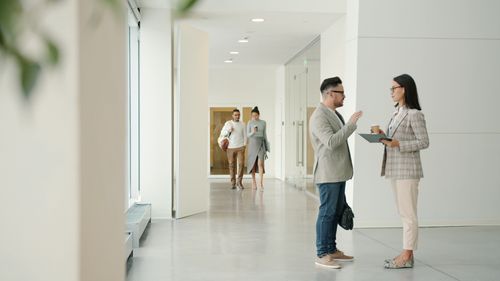 Free Professionals engage in conversation inside a bright, modern office hallway. Stock Photo