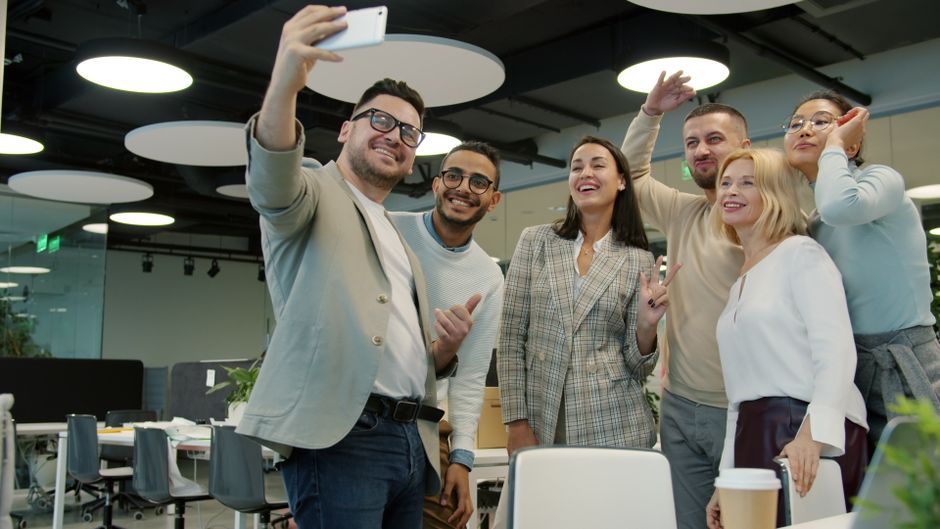Un grupo de compañeros de trabajo alegres se toman una selfie en un entorno de oficina moderno.