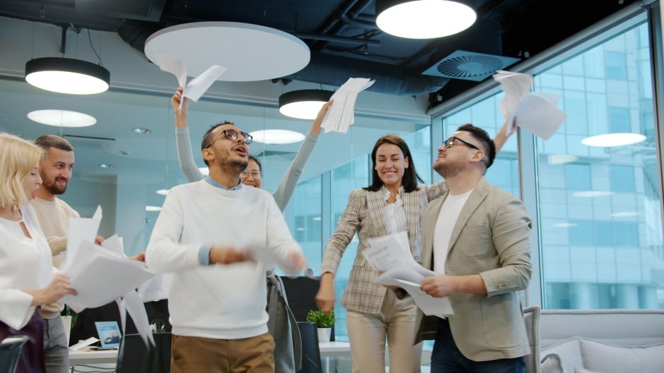 Un grupo diverso de profesionales celebrando el éxito en un entorno de oficina diáfano.