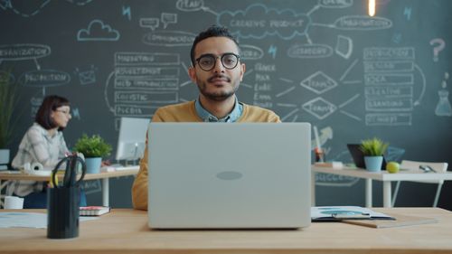 Free Focused young professional working on laptop in a creative office with chalkboard wall. Stock Photo