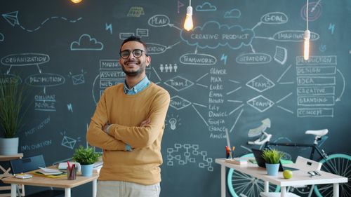 Free Young entrepreneur smiling in a modern office with creative chalkboard. Stock Photo
