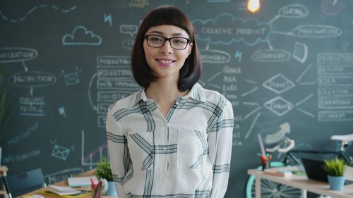 Free Young woman smiling in modern office with creative chalkboard background. Stock Photo