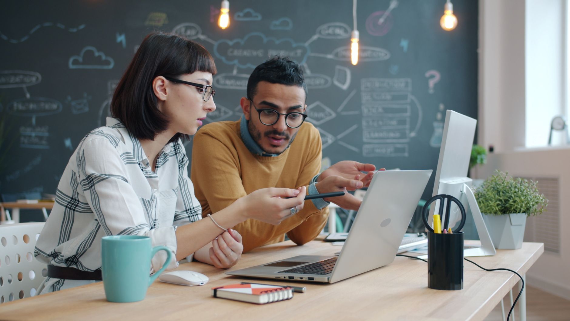 Two colleagues leaning over a laptop discussing notes during an interview prep session