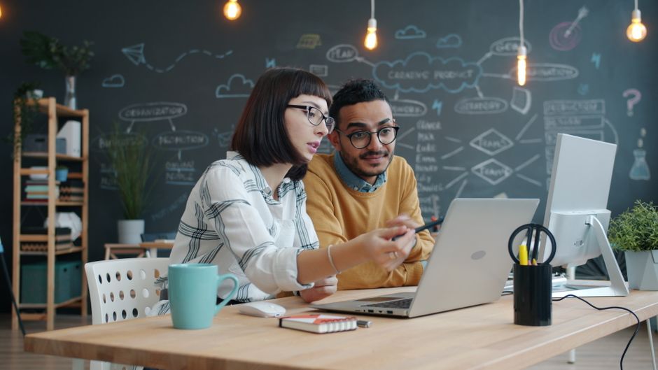 Dos compañeros de trabajo colaborando en un proyecto en una oficina moderna.