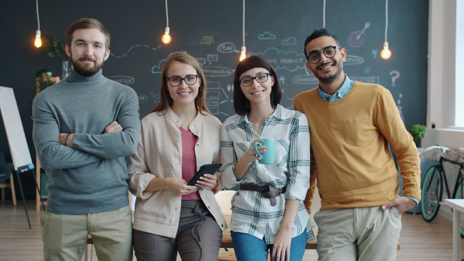 Un grupo diverso de jóvenes profesionales sonriendo en un espacio de trabajo creativo.