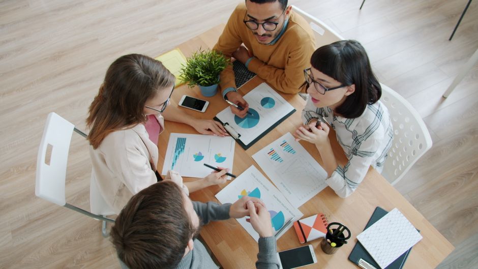 Vista aérea de un equipo diverso en una sesión de lluvia de ideas con gráficos y diagramas sobre una mesa.