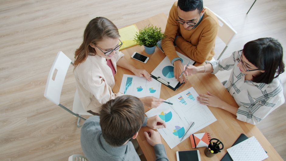 Equipo diverso que colabora en el análisis de datos mediante gráficos y teléfonos inteligentes.