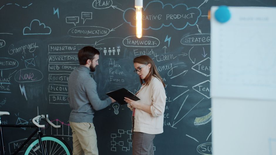 Dos profesionales discutiendo ideas creativas en una pizarra en una oficina.