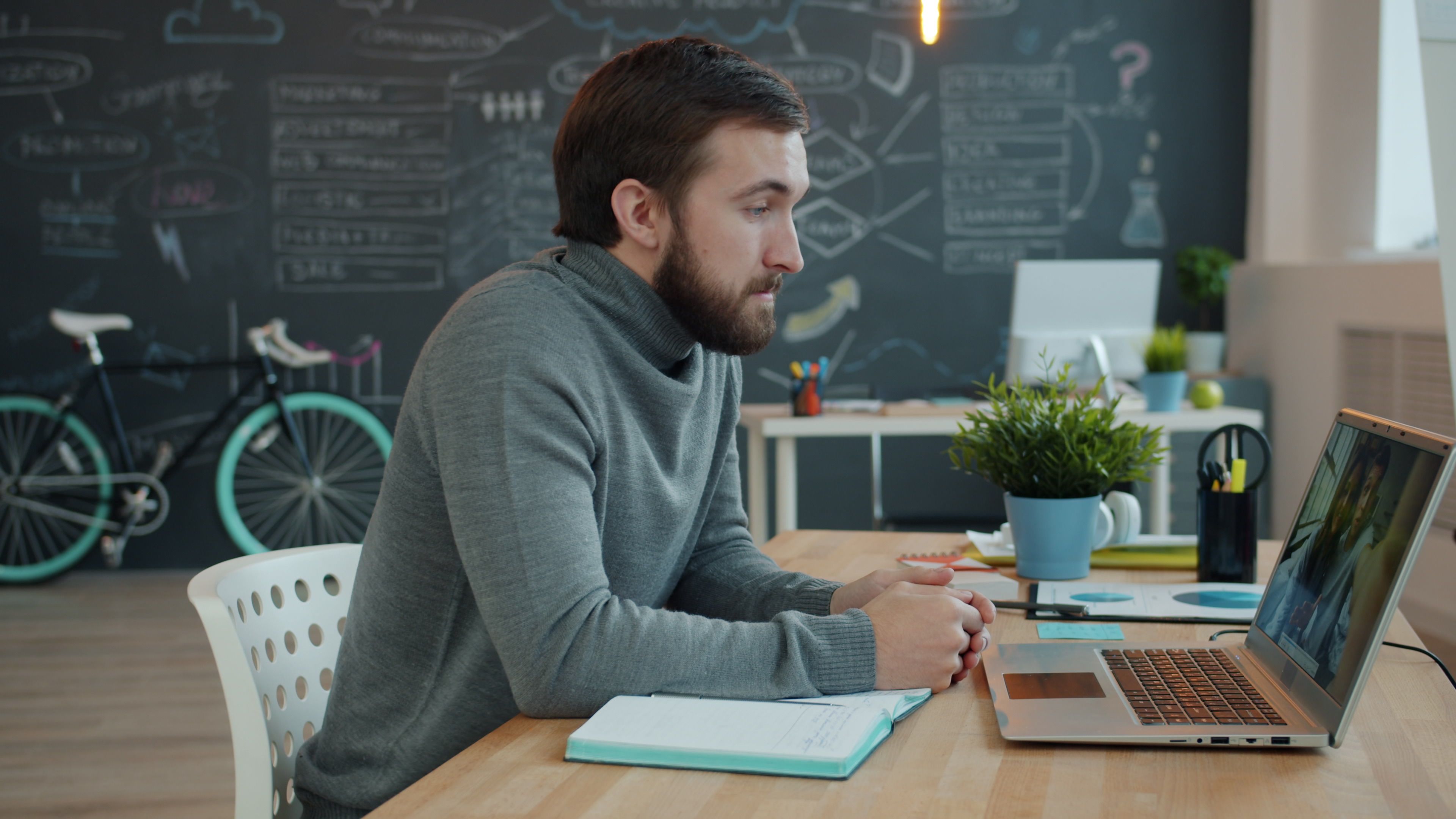 Young man engaged in virtual meeting from creative workspace with laptop.