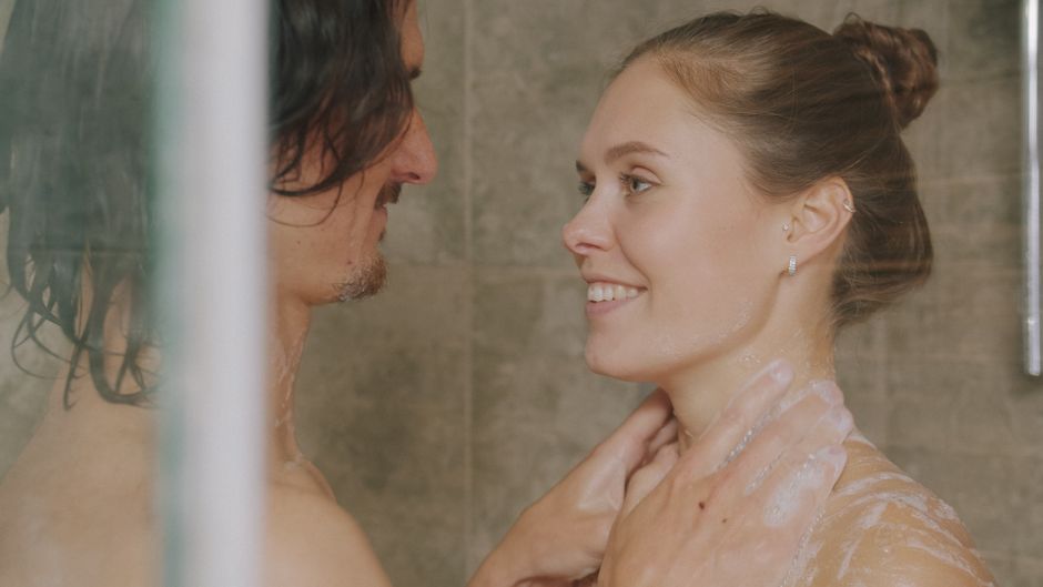 A couple enjoys a warm, intimate shower together, embracing and smiling.
