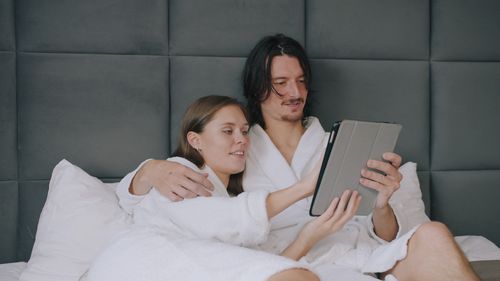 Free A couple in bathrobes using a tablet in bed, enjoying a cozy indoor setting. Stock Photo