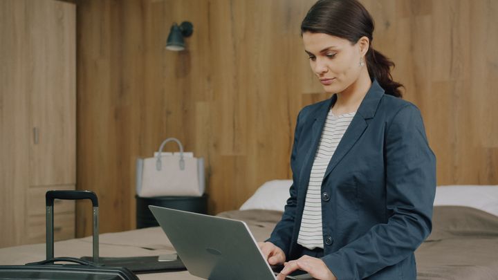 Mujer escribiendo en un portátil en una habitación de hotel
