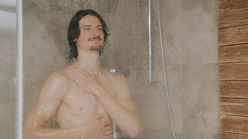 Free Adult male enjoying a shower with natural stone tiles in a modern bathroom setting. Stock Photo