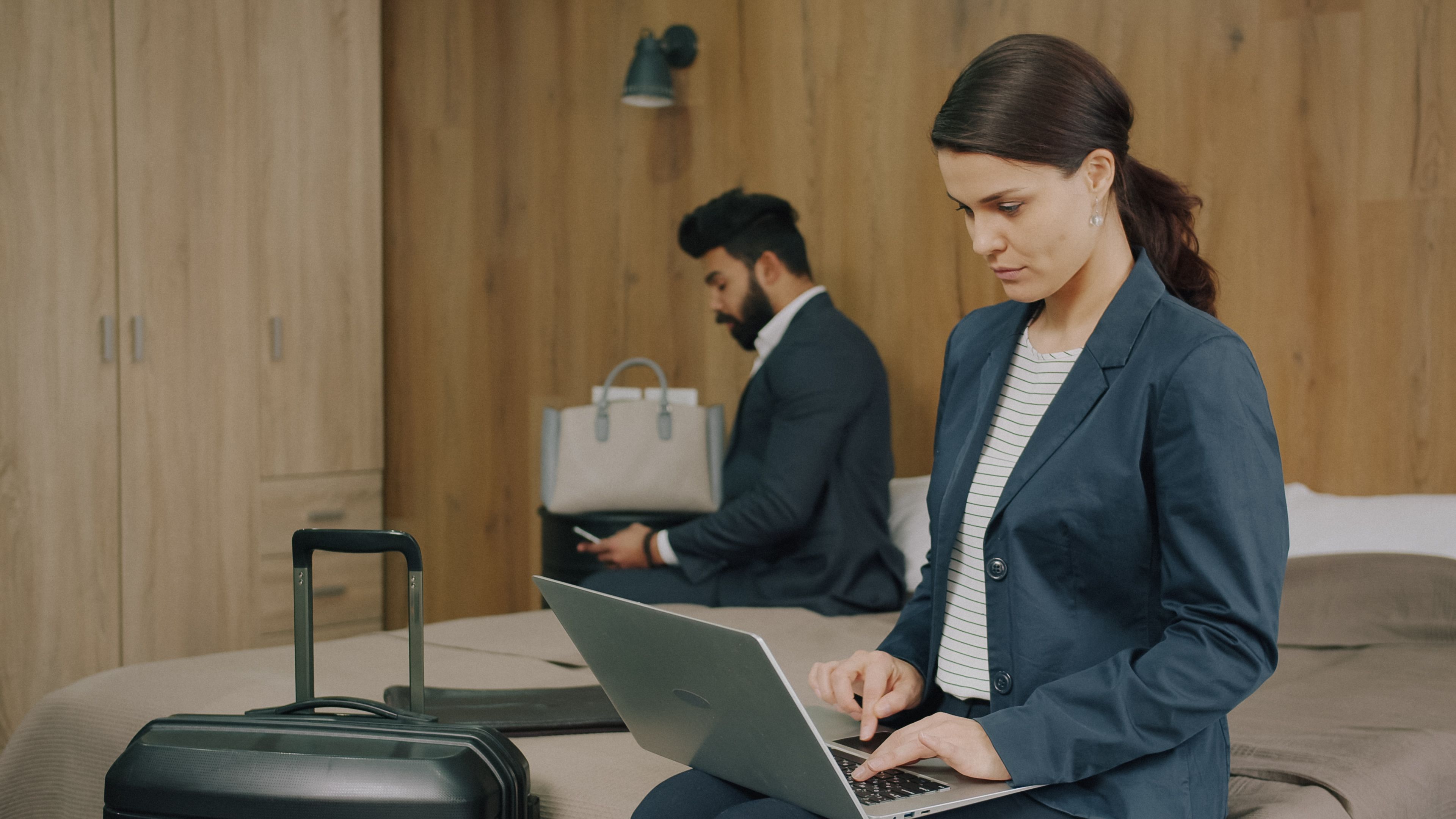 Business professionals using laptops in a hotel room, focused on work.