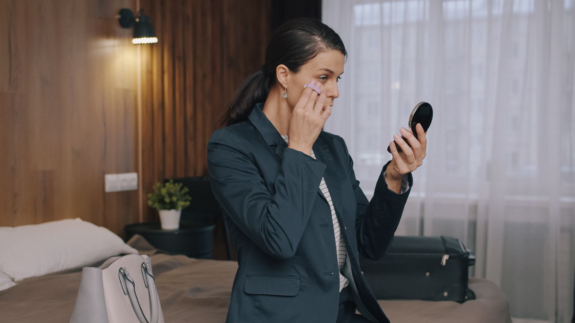 A businesswoman in a hotel room preparing for a meeting, using a compact mirror.