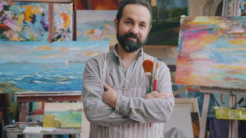 Free Portrait of a male artist in a studio with vibrant paintings, exuding creativity and inspiration. Stock Photo