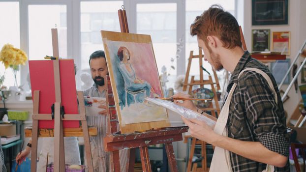 Two artists working on paintings in a well-lit art studio.