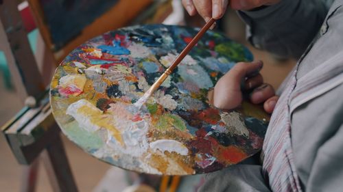 Free A close-up of an artist's hand mixing paint colors on a vibrant palette. Stock Photo