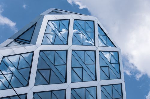 Free Close-up view of a modern building with geometric glass facade reflecting fluffy clouds in the sky. Stock Photo