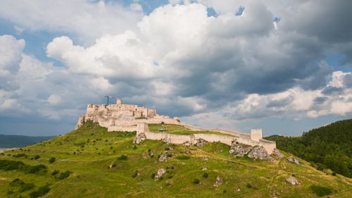 Free Dramatic clouds hover over the historic Spis Castle, a UNESCO site in Slovakia, set against lush greenery. Stock Photo