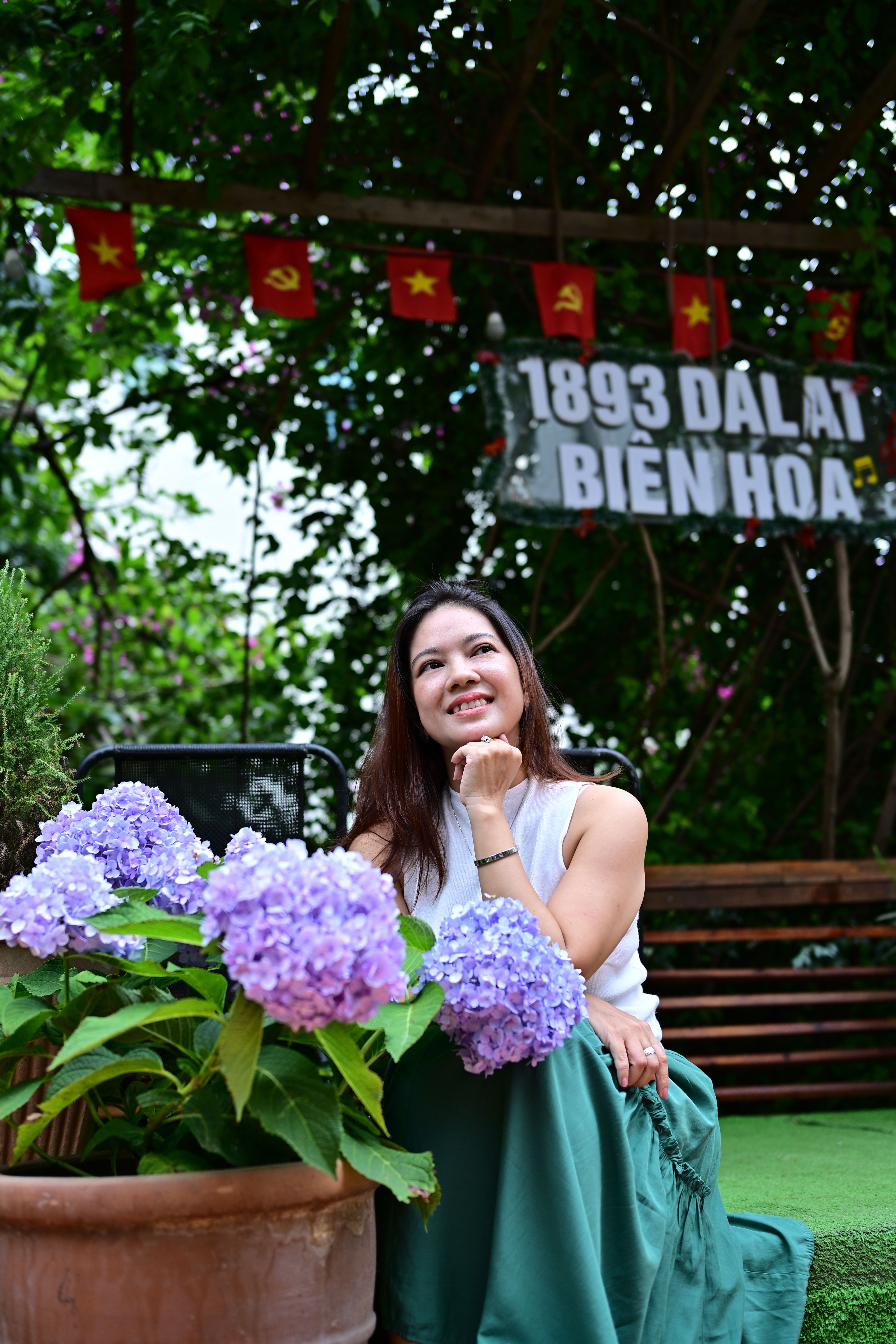 Woman with hydrangeas sitting outdoors in a garden with vibrant decor and flags.