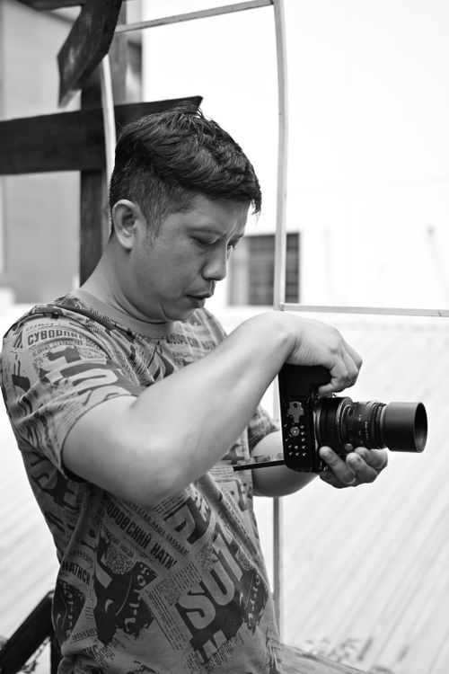 Free Black and white image of a male photographer adjusting his camera outdoors. Stock Photo