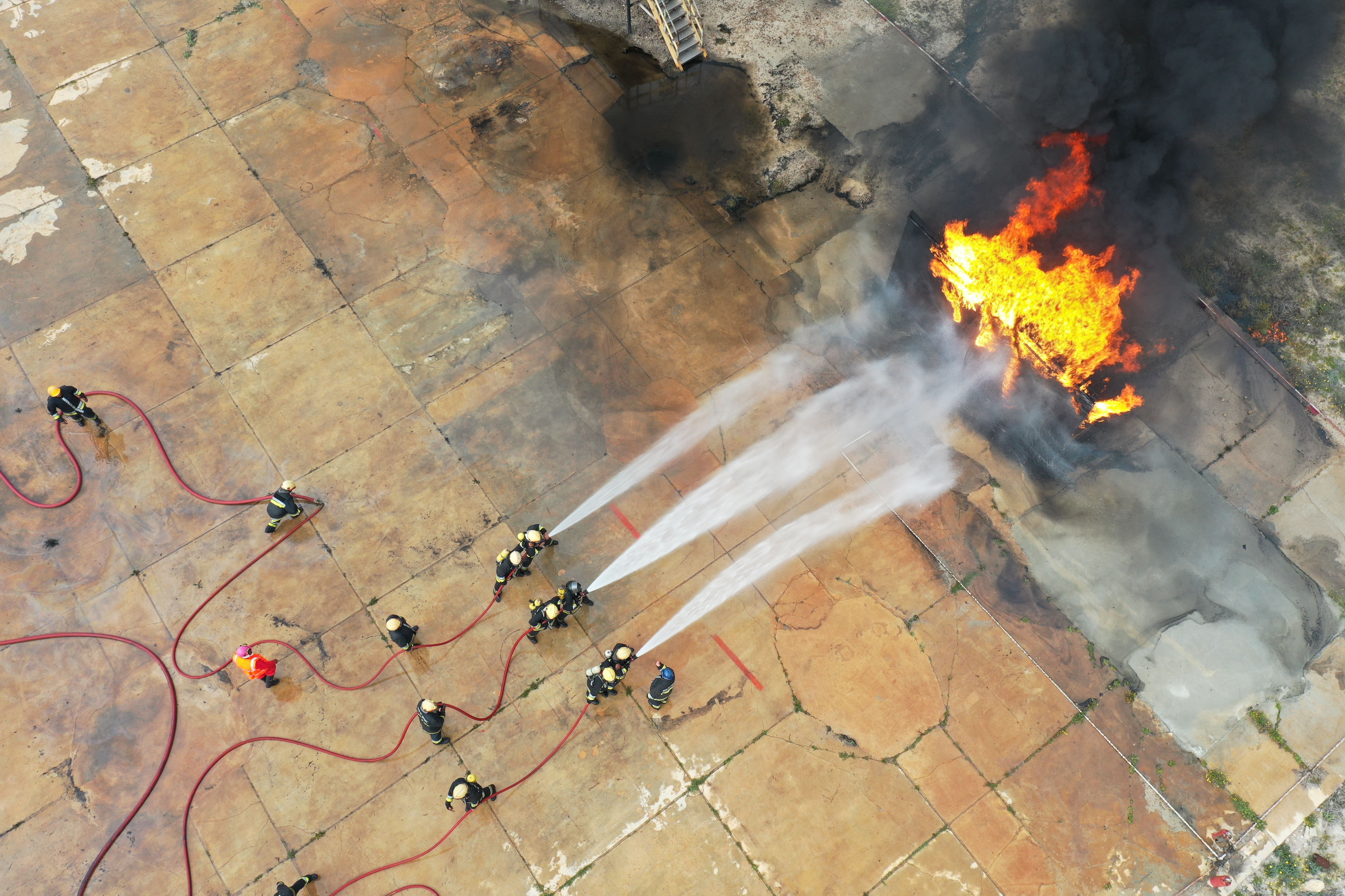 Aerial view of firefighters battling flames and thick smoke.
