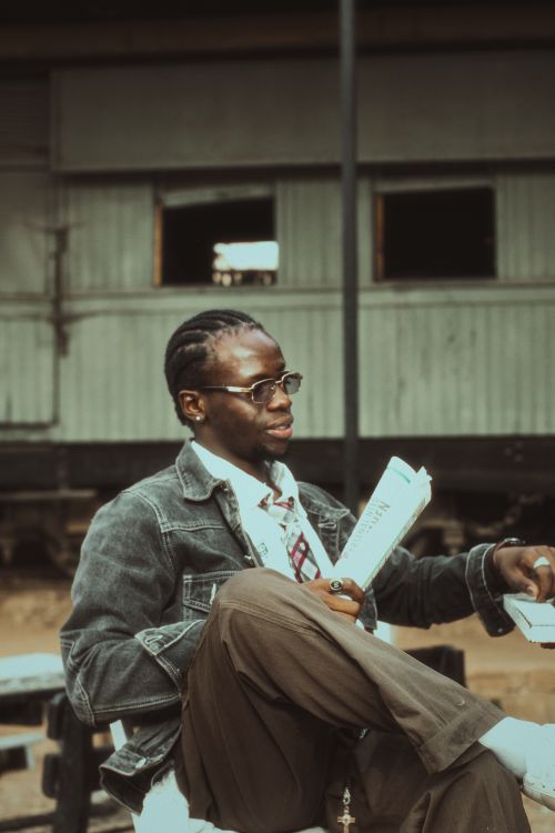 Free A stylish young man reads a newspaper in a vintage train station environment. Stock Photo