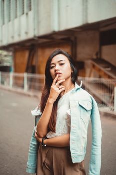 一位穿着牛仔夹克的时尚女士在街头自信摆姿，这张城市风格摄影采用了景深效果