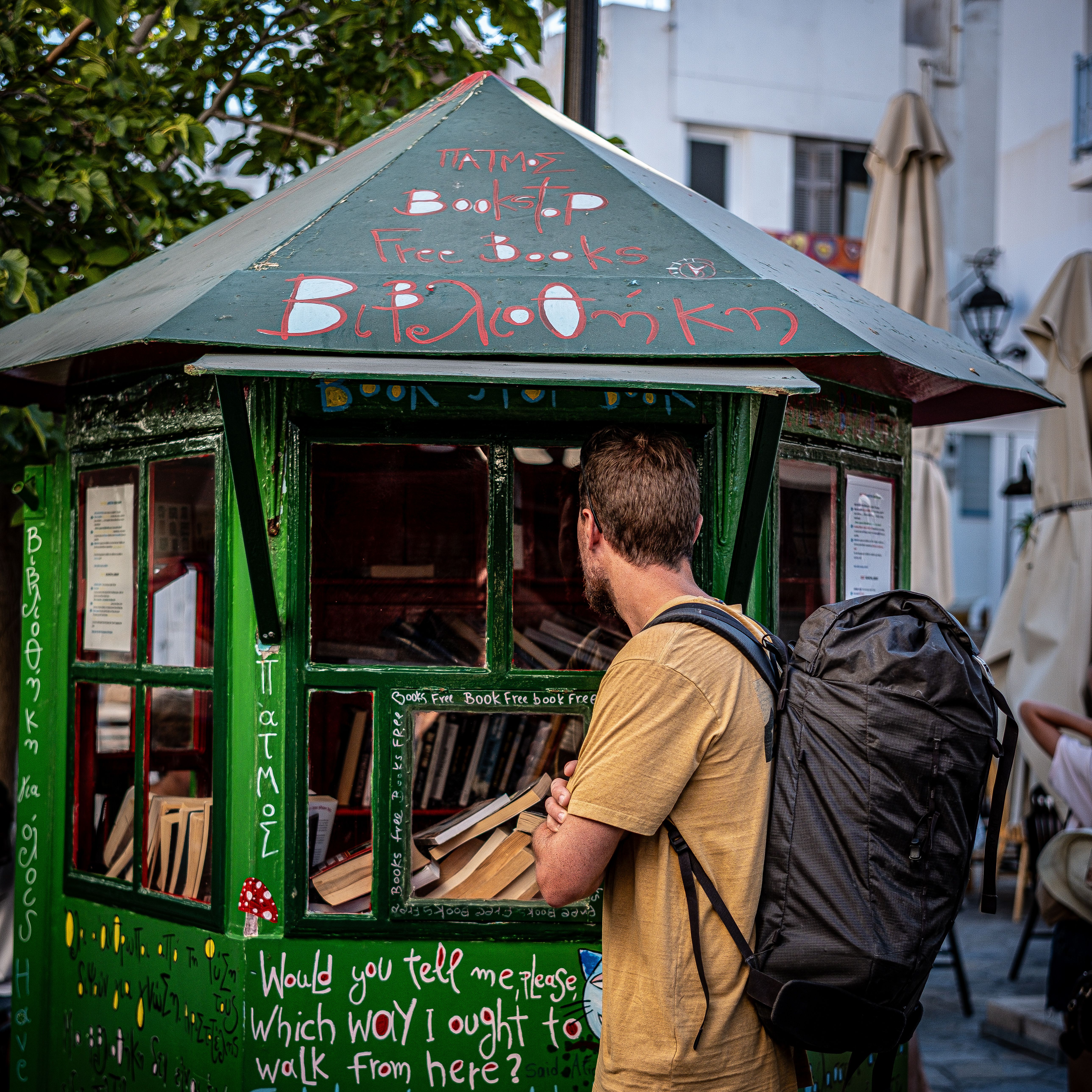 Traveler browsing a free book kiosk in Greece. Outdoor reading spot.