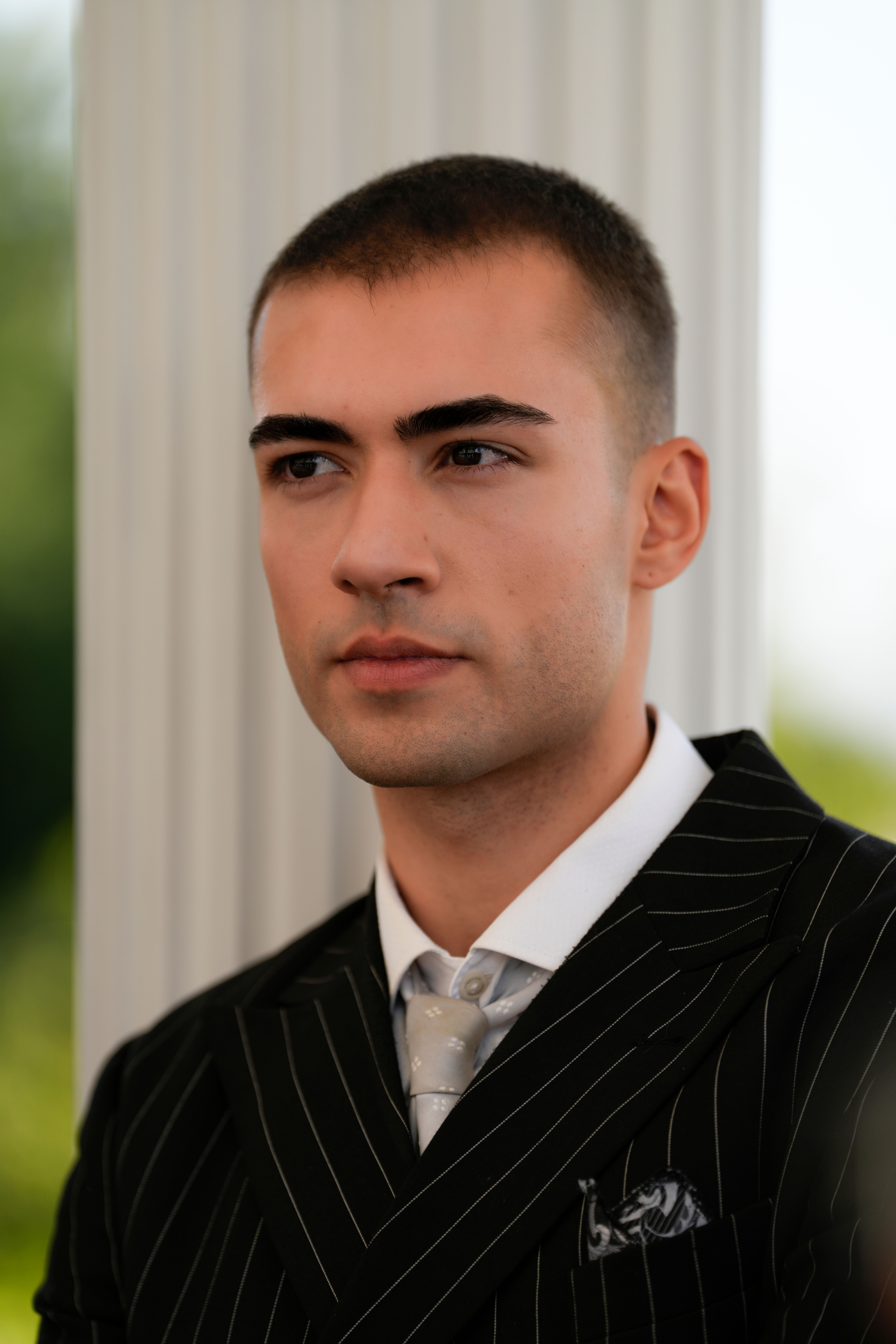 Professional portrait of a confident young man in a striped suit against a subtle background.