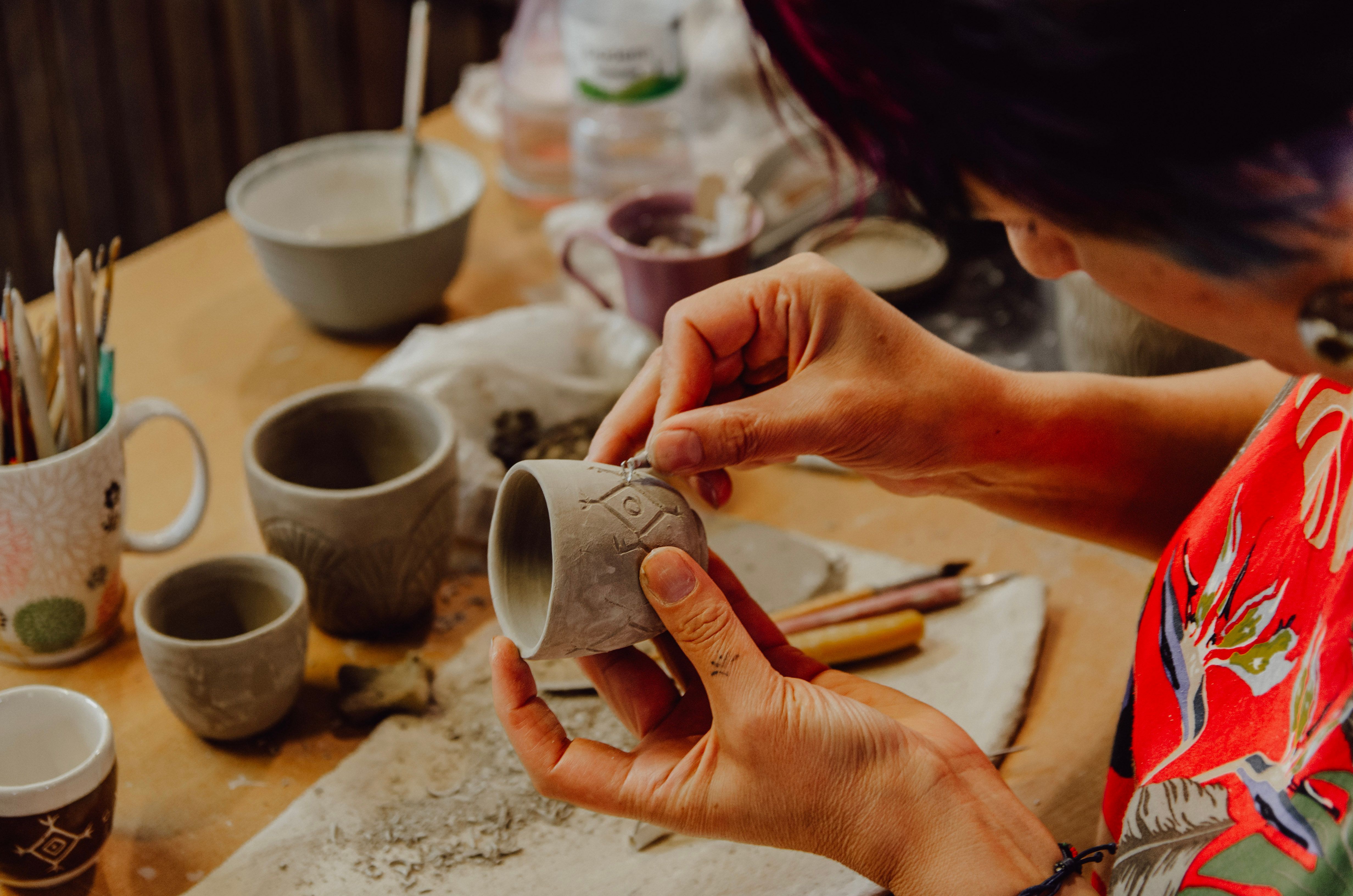 Close-up of ceramic artist crafting a patterned cup in a pottery studio, showcasing creativity and skill.