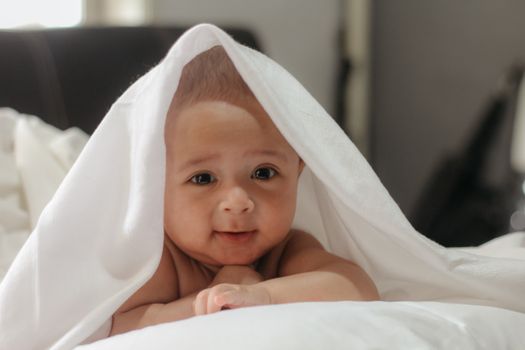 A cute baby peeks from under a soft white blanket, expressing warmth and joy.