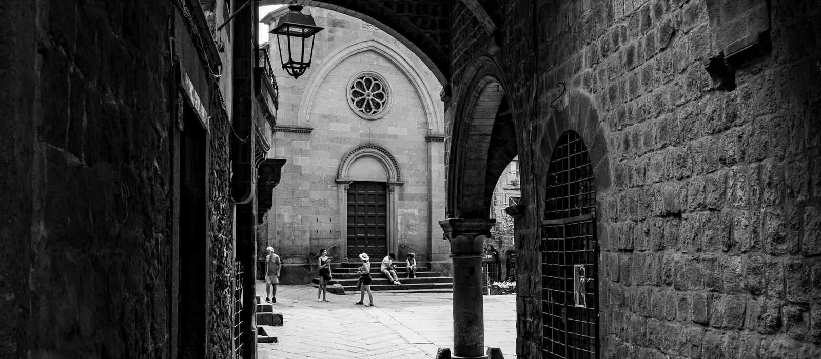 Black and white photo of a historic alley in Viterbo, Lazio, featuring archways.
