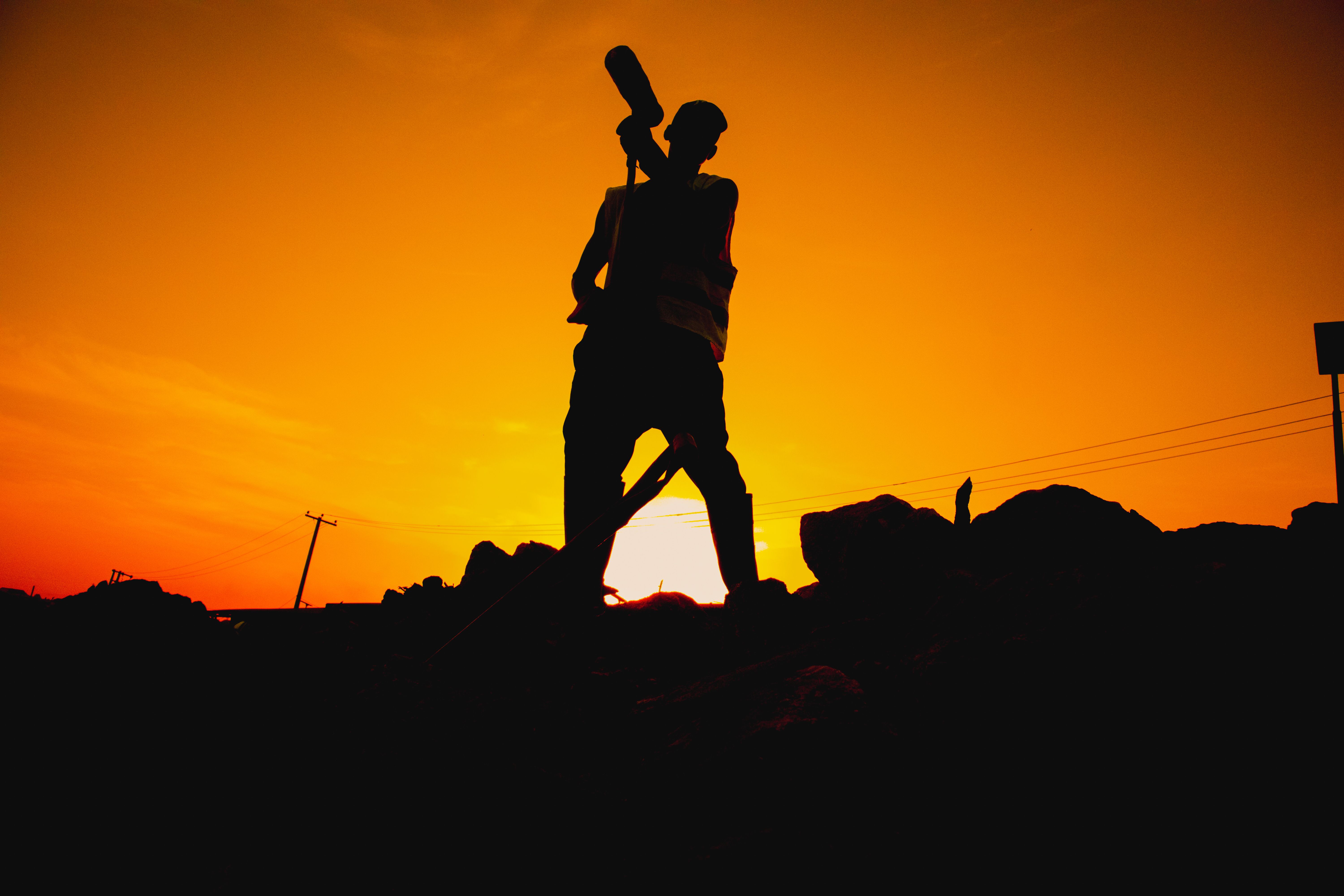 Silhouette of a worker with a shovel against a vibrant sunset. Powerful and dramatic.