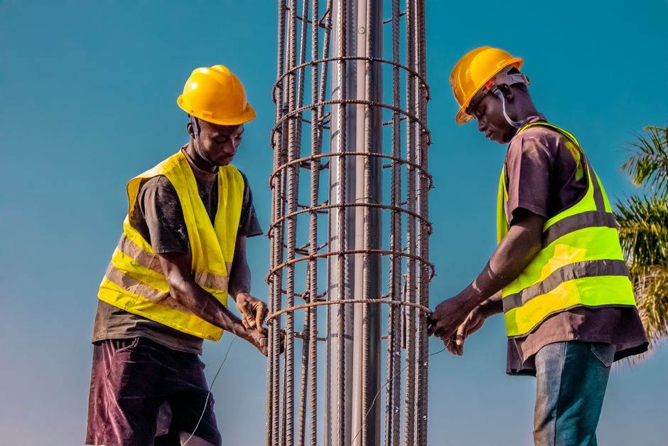 Two construction workers wearing safety gear securing steel rebar structure outdoors.